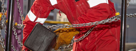 Repair of the playground. A log with chains is being repaired by a worker in a red suit and leather...