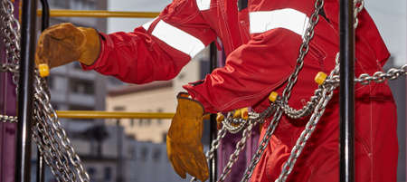 Repair of the playground. A log with chains is being repaired by a worker in a red suit and leather...
