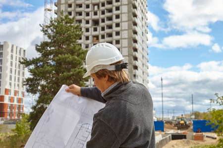 An engineer in a white helmet. A man with a drawing in his hands on a construction site.