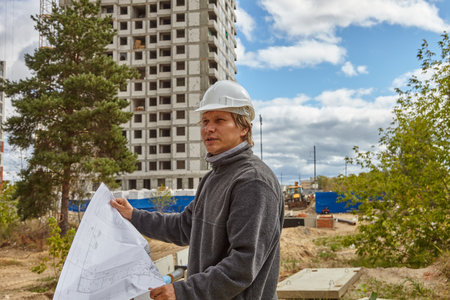 An engineer in a white helmet. A man with a drawing in his hands on a construction site.