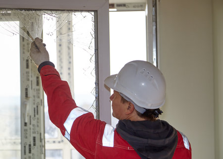 A worker in a white helmet. An engineer examines a broken window.