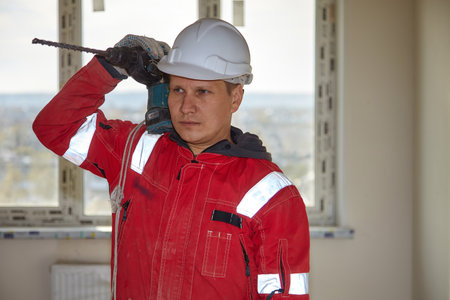 A builder in a white helmet drills a wall with a drill. Laying of communications on the construction site.の写真素材