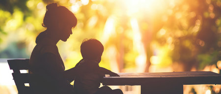 Silhouette of mother and son sitting on a bench in the park.の素材