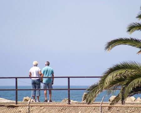 Mature couple looking out over the ocean holding hands.の写真素材