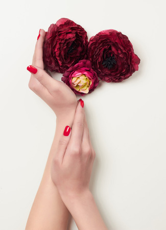 Closeup cupped hands with red manicure and red flowers.beauty woman hands with artificial flowerの写真素材