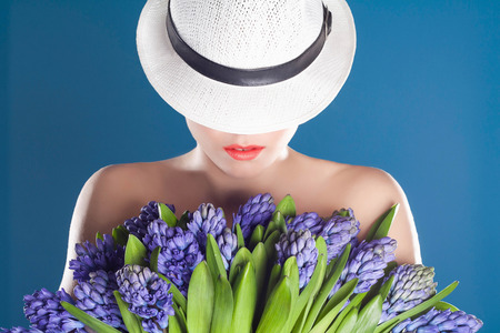 close-up portrait of beautiful woman in hat with flowers. Pretty Girl with big bouquet.blue backgroundの写真素材