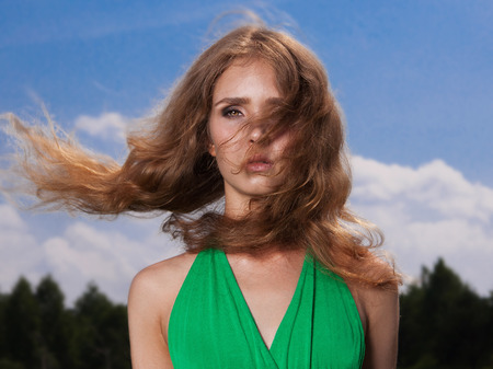 Beautiful blond girl in green dress on the field in summer forest.beauty young woman.Wind flying hairの写真素材