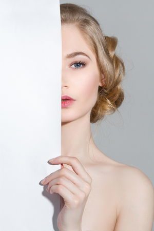 young blonde sexy woman holding paper.girl hide empty card board paper with copy space.beauty girl with hairstyleの写真素材