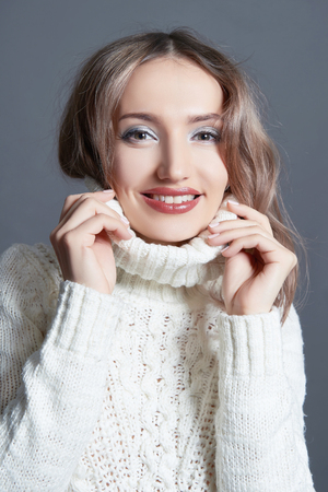 happy smiling winter style young woman.Cheerful blonde girl in sweater isolated on the gray backgroundの写真素材