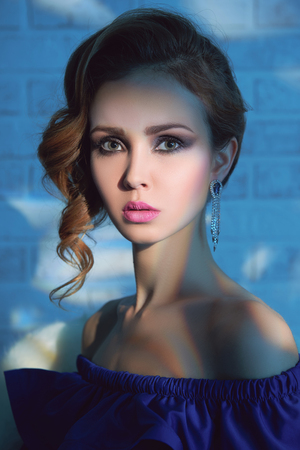 beautiful blonde young woman in blue dress stay over bricks wall at home.beauty elegance model with make-up and jewelryの写真素材