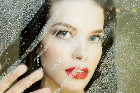Young woman behind wet window.autumn Beautiful Girl with glass