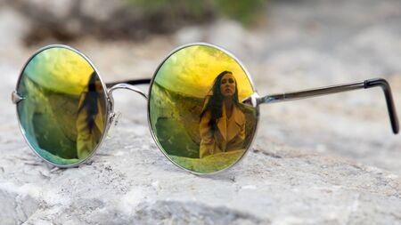 A woman's reflection in glasses.girl sitting on mountains in mirror sunglasses