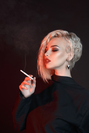 Young sexy woman smoking cigarette. blonde girl with curly hair and make upの写真素材