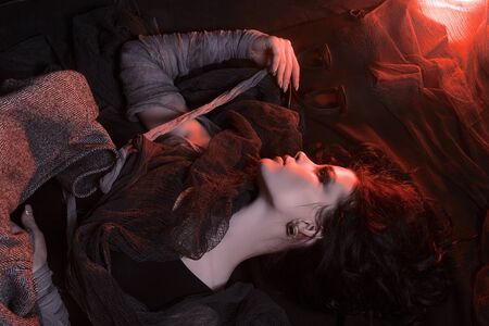 beautiful young woman with make-up on the floor.halloween style smokey eyes beauty girl wrapped in rags. mummy in red color lightの写真素材