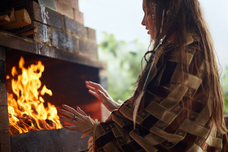 girl is warming her hands by the fire in the fireplace. young woman by the fireの写真素材