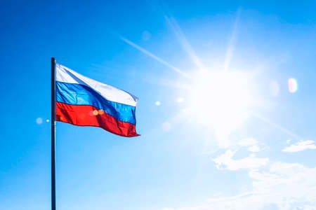 Russian flag on blue sky background with sun flare and raysの写真素材