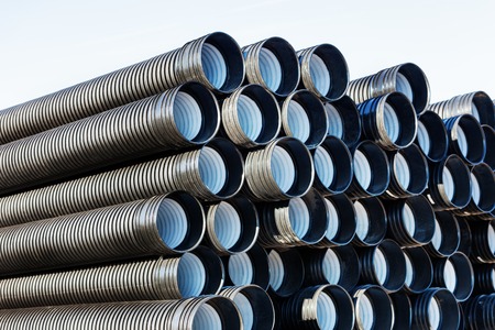 stacks of black pvc plastic pipe outdoors outside the warehouseの写真素材