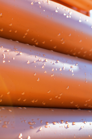 Abstract close up of a stack of orange plastic pipes on construction with water drops for plumbingの写真素材