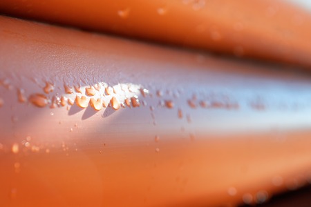 Abstract close up of a stack of orange plastic pipes on construction with water drops for plumbingの写真素材