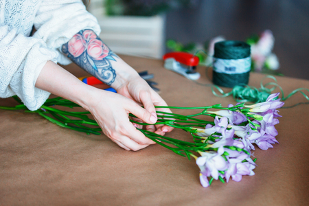 close up table top view of female shop assistant making bouquet with purple crocus and white roses. Flower shop and floristic design master class concept on painted blue wall loft styleの写真素材