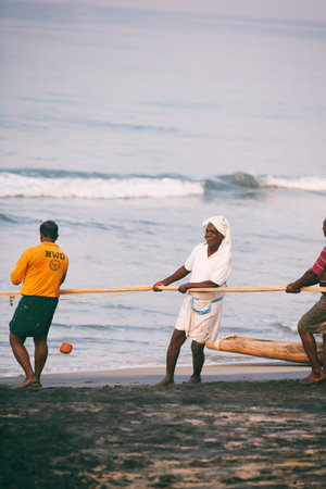 Varkala, India - February 09, 2016: Fishing net with many fishermen on backside the boat. Odayam beach, Varkala, Indiaのeditorial素材