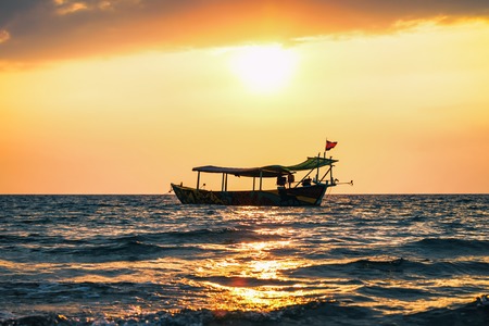 Bright red sunset on the beach with fishing boat in Cambodia, Sihanoukville, sun beamの写真素材