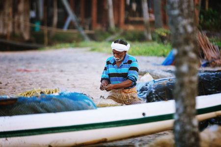 Varkala, India - February 09, 2016: Portrait of happy Indian fisherman unravels fishing nets and tackle while sitting in a boat, Kerala India Fishery Gulf. Odayam beach, Varkala, Indiaのeditorial素材