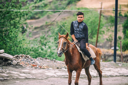 Lahic, Azerbaijan - July 18, 2015: Azeri boy riding a horse in the Street on cobblestone Huseynov street, the main street of Lahic mountainous village of Azerbaijan, with buildings, shops and people.のeditorial素材