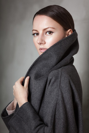 high fashion portrait of young elegant woman in studio on greyconcrete vintage wall. Grey coatの写真素材
