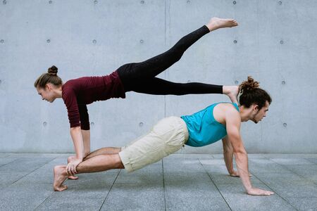 Male and female couple practicing acro yoga outdoors on grey wall background. Acroyoga concept for...