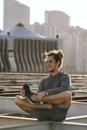 Positive young european man crossing legs in lotus pose croosed legs on blurry urban residential...