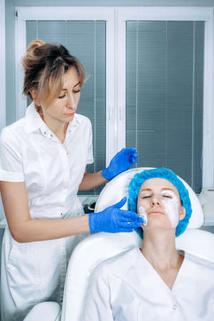 Cosmetologist is applying cream with anesthesia on patient's face, portrait closeup view. Preparing skin for biorevitalization procedure in cosmetology. Woman in beauty clinic with doctor beautician.の写真素材