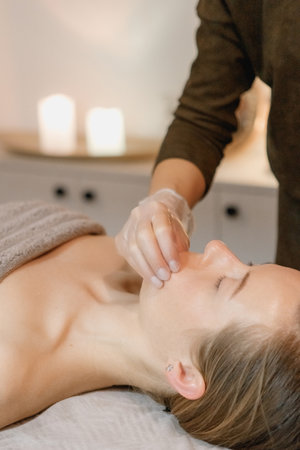 buccal facial massage, close-up, cosmetologist makes woman a procedure on a massage table in a spa salonの写真素材