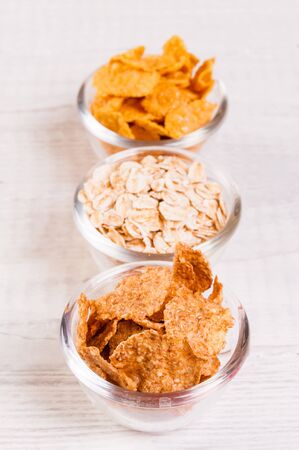 assortment breakfast cereals in small glass dishes on wooden table, almond nuts close up