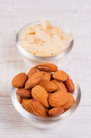 Almond nuts and sliced shavings in small glass dishes on a wooden tableの写真素材