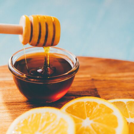 Honey in jar with honey dipper and fresh lemon on blue background. Toned.の写真素材