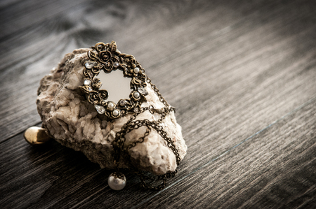 Old vintage oval mirror necklace on a stone fashion objects on wooden table. Filtered image, tonedの写真素材