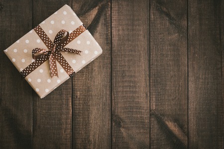 Box in craft paper, eco paper on the wooden table. Top view. Brown paper wrapped gift box with satin ribbon bow on a old rustic wooden background. Background for your design. Retro filter. Copy space for your textの写真素材