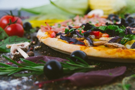 Italian pizza with mozzarella, black olives, prosciutto and tomatoesの写真素材