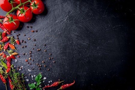 Fresh cherry tomatoes on a black background with spices with slate plate. Top view with copy space.の写真素材