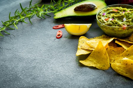 Guacamole bowl with ingredients and tortilla chips on a stone table. Selective focus. Copyspace for your text.の写真素材