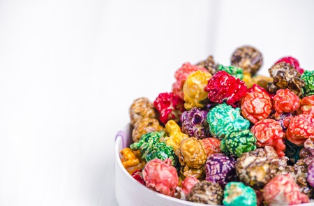 Brightly Colored Candied Popcorn, white background. Horizontal image of Junk food, fruit flavored popcorn in light pink bowl. Colorful, rainbow, candy coated popcorn. Shallow focus on popcorn in bowlの写真素材