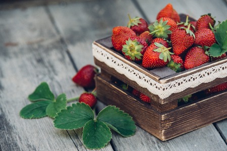 Fresh juicy strawberries with leaves. Rustic wooden box and handmade lace. Retro magazine picture. Strawberry with copy space.