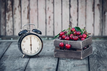 Summer Time, red cherry and an Alarm Clock on an Old Wooden Table.の写真素材