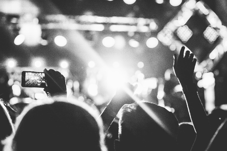 Audience with hands raised at a music festival and lights streaming down from above the stage. Soft focus, blurred movement. Black and white.の写真素材