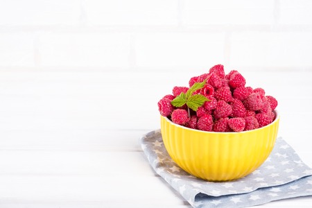 Fresh raspberry in a modern yellow bowl on light background.