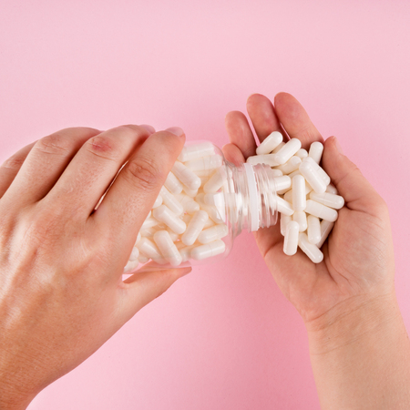 Hands hold pills isolated on pastel coloured background. Medication and prescription pills flat lay...