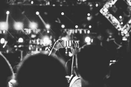 Audience with hands raised at a music festival and lights streaming down from above the stage. Soft focus, blurred movement. Black and white.の写真素材