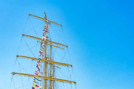 Colorful nautical sailing flags flying in the wind from the lines of a sailboat mast backlit in bright blue sky by the sun.の写真素材