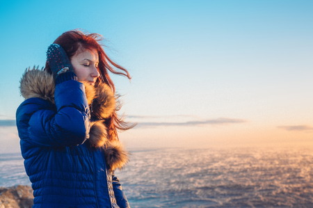 Young beautiful girl woman enjoying sunset at stormy sea in winter.の写真素材